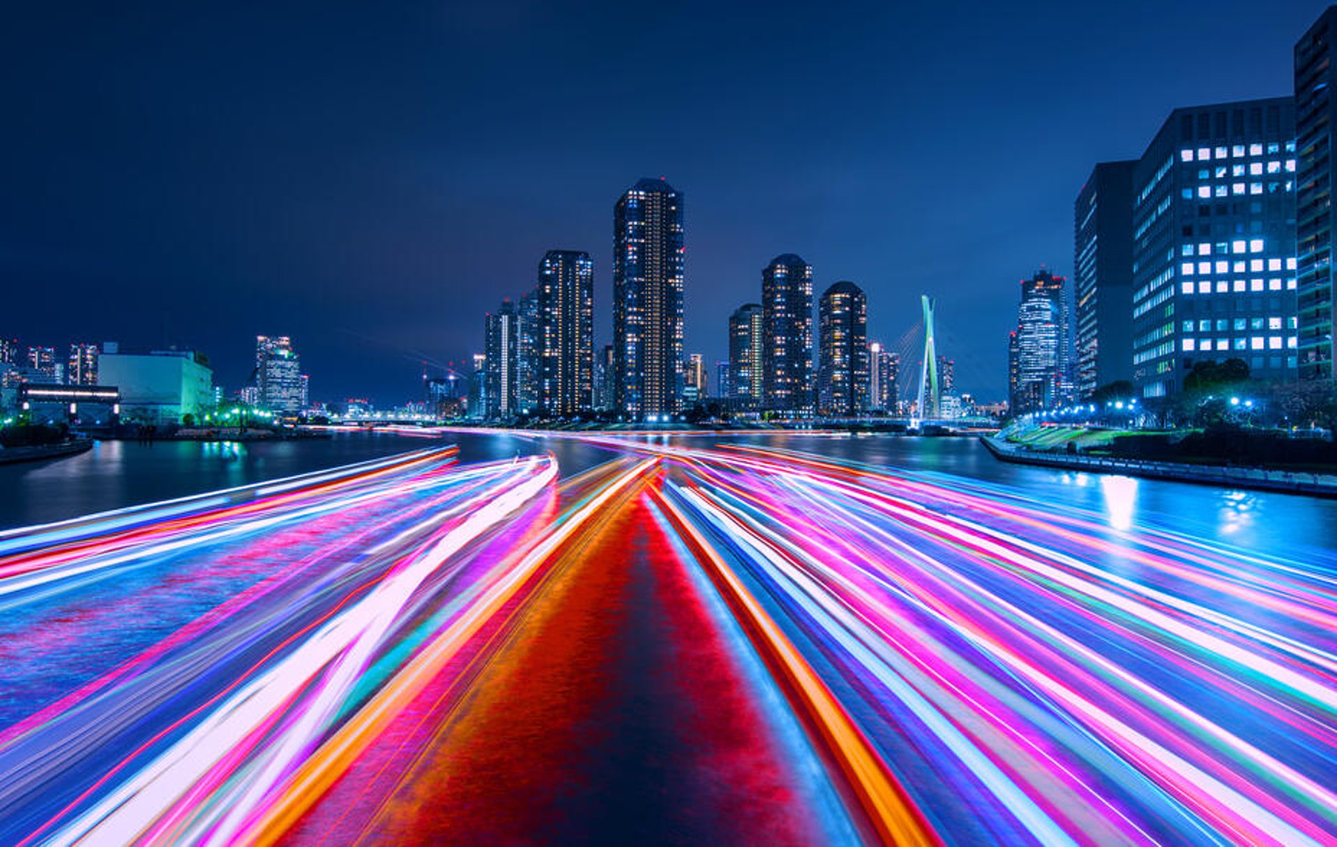 A night view of Tokyo over the Sumida River with houseboat light trails.