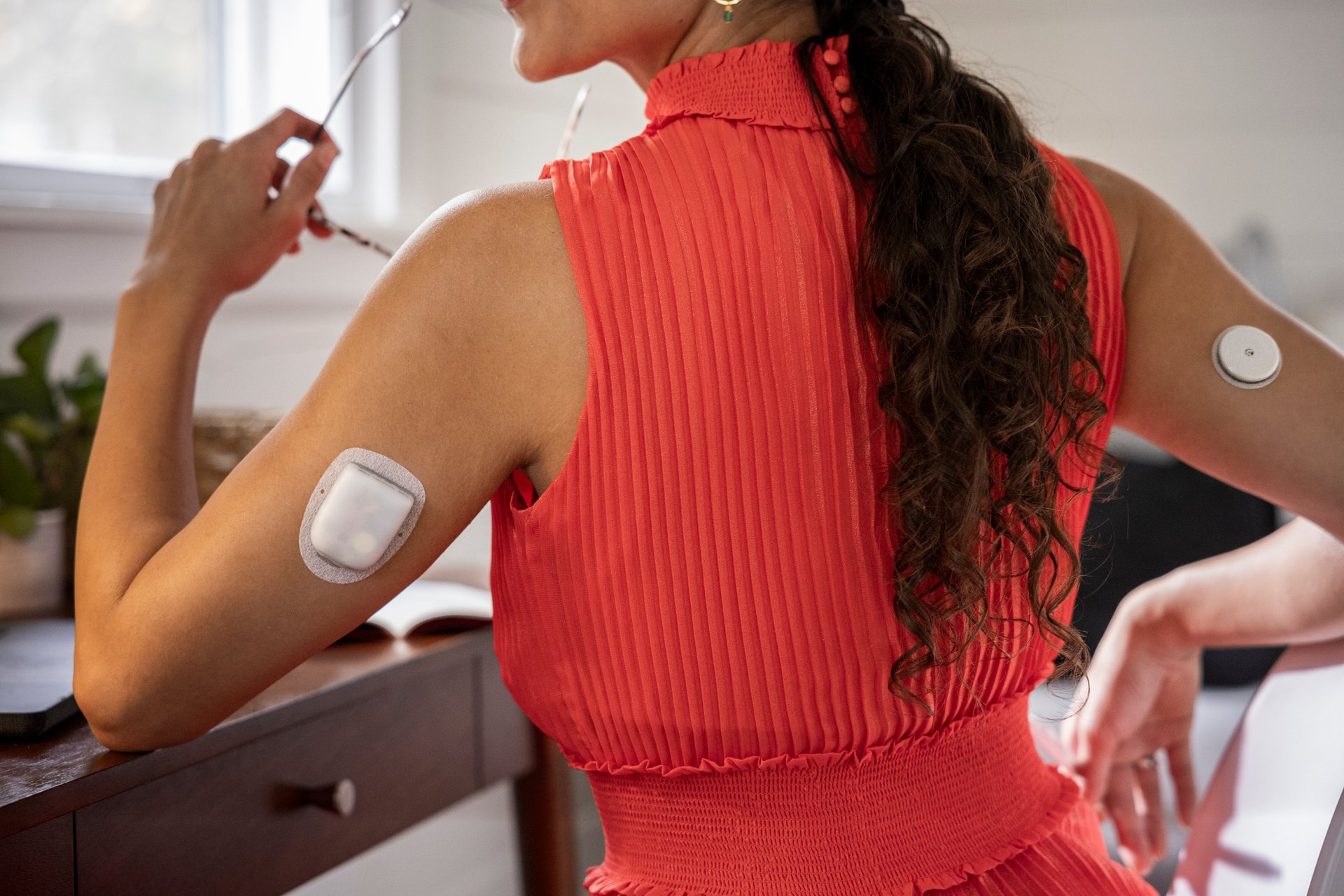 A person in a red blouse with an automated insulin device attached to their arm