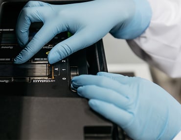 A person wearing blue gloves is adjusting a component of an Illumina sequencing machine.