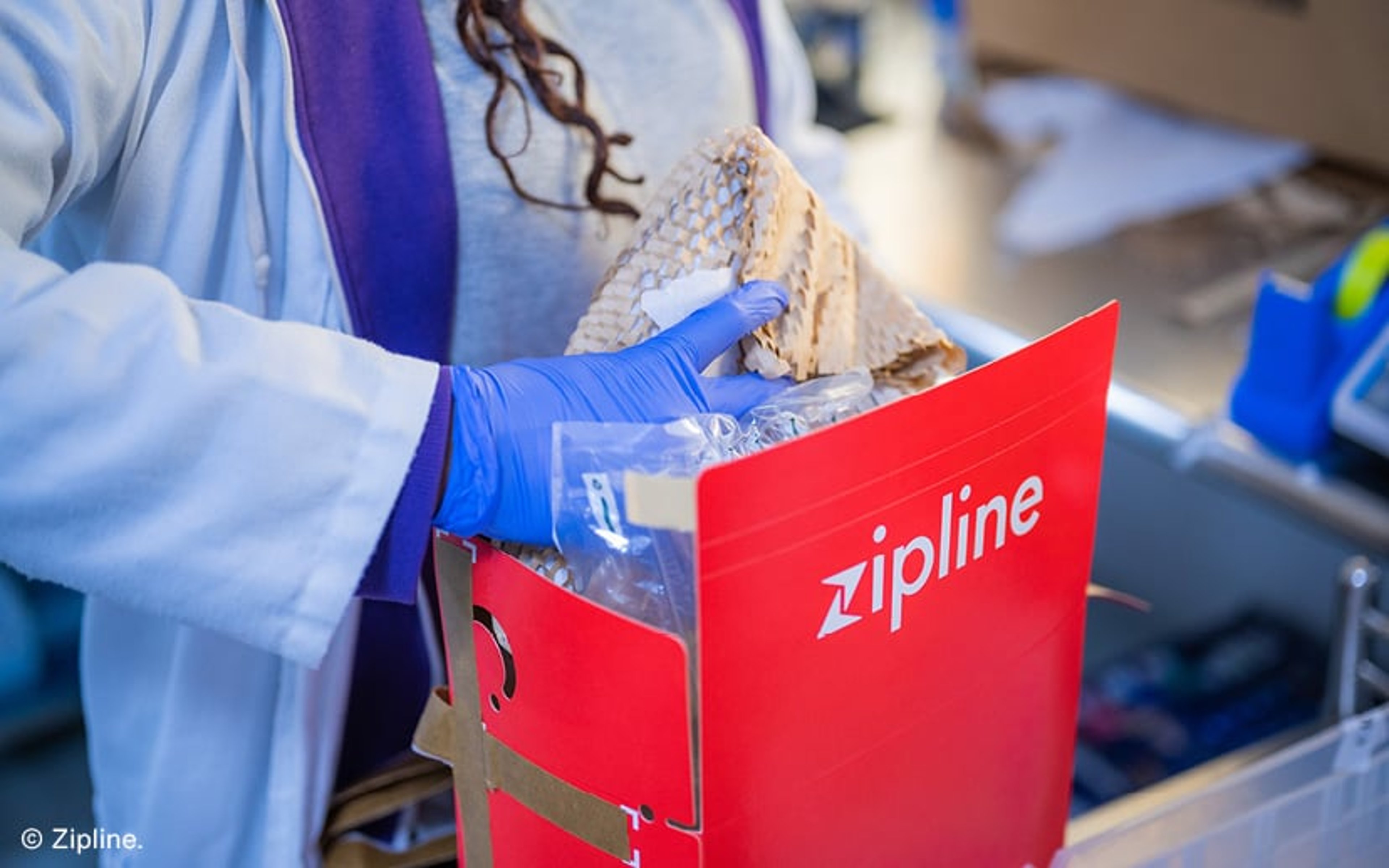 A person places a package inside a red box branded Zipline. © Zipline.