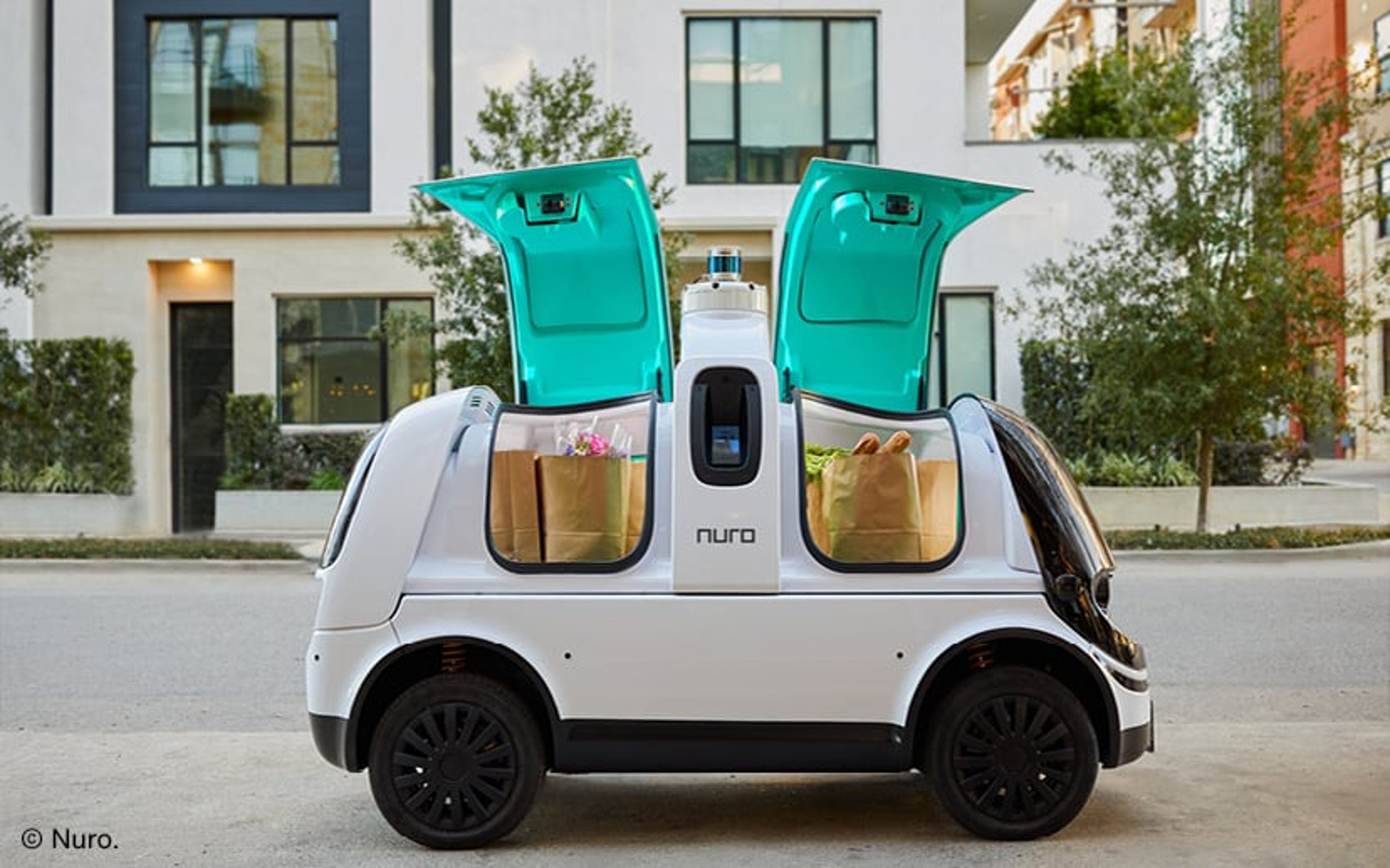 A driverless electric delivery vehicle with its doors open revealing packages. © Nuro.