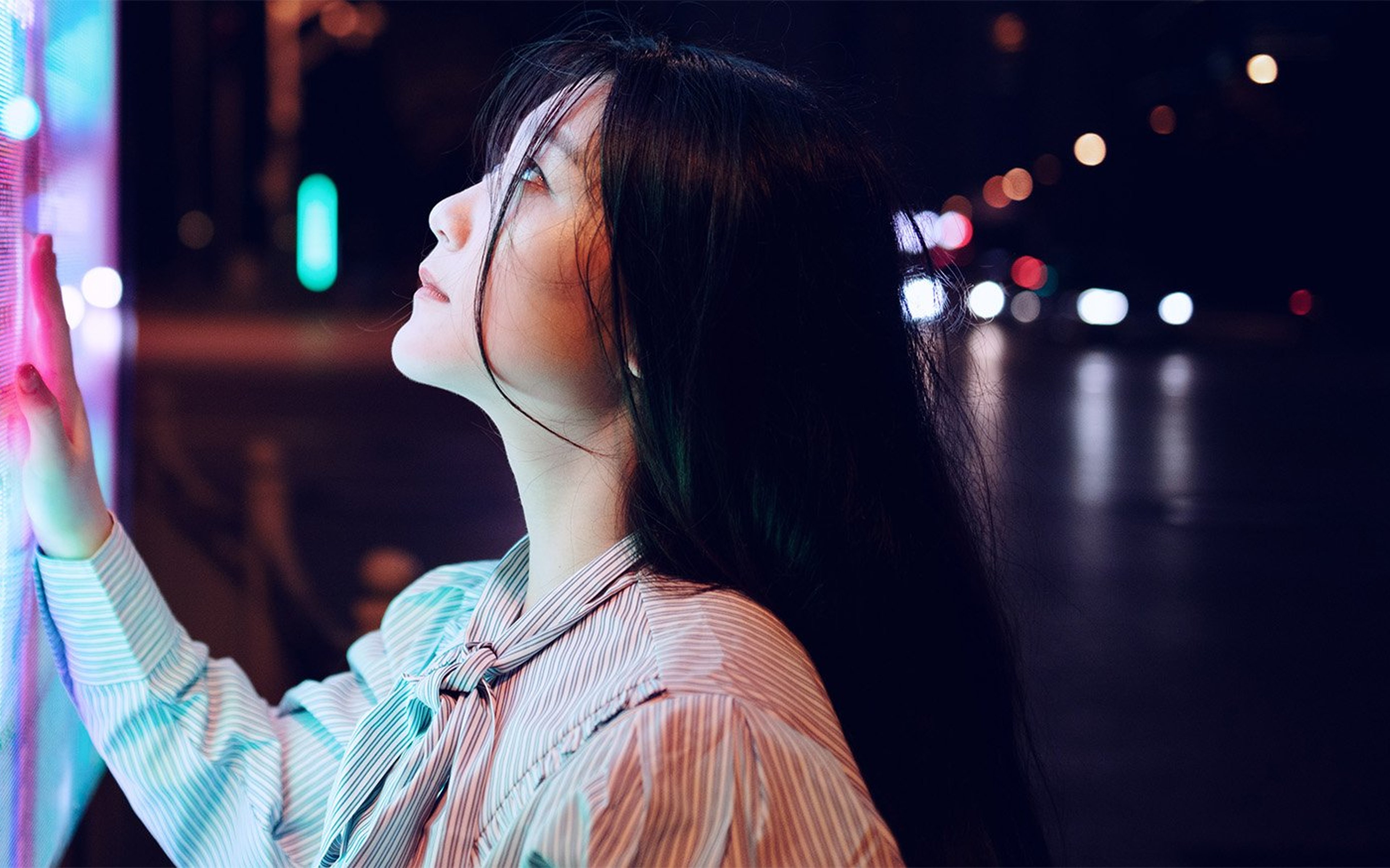 A person toucing a large multicoloured screen in a dark street in an Asian city