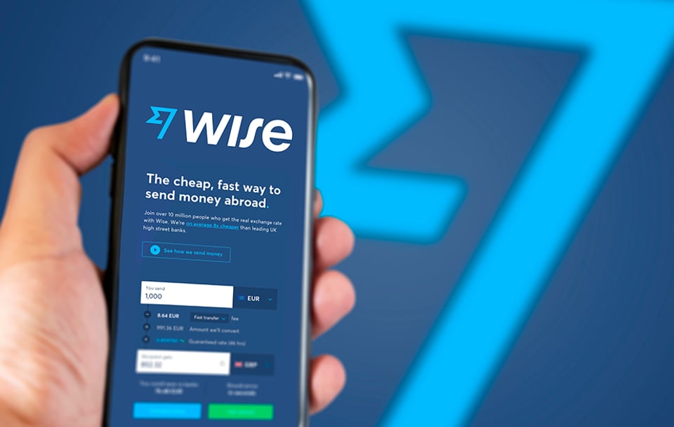 Hand holding phone showing Wise app, blue background with Wise logo